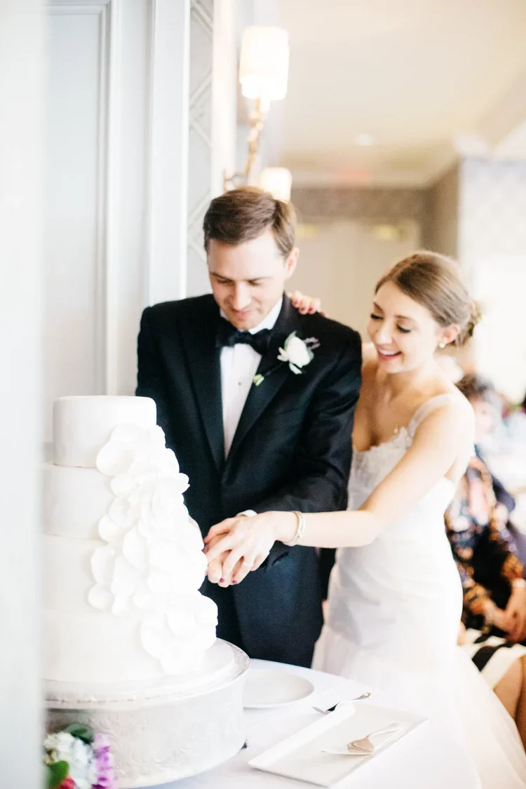 A newlywed couple, dressed in wedding attire, cutting a white wedding cake at their reception.