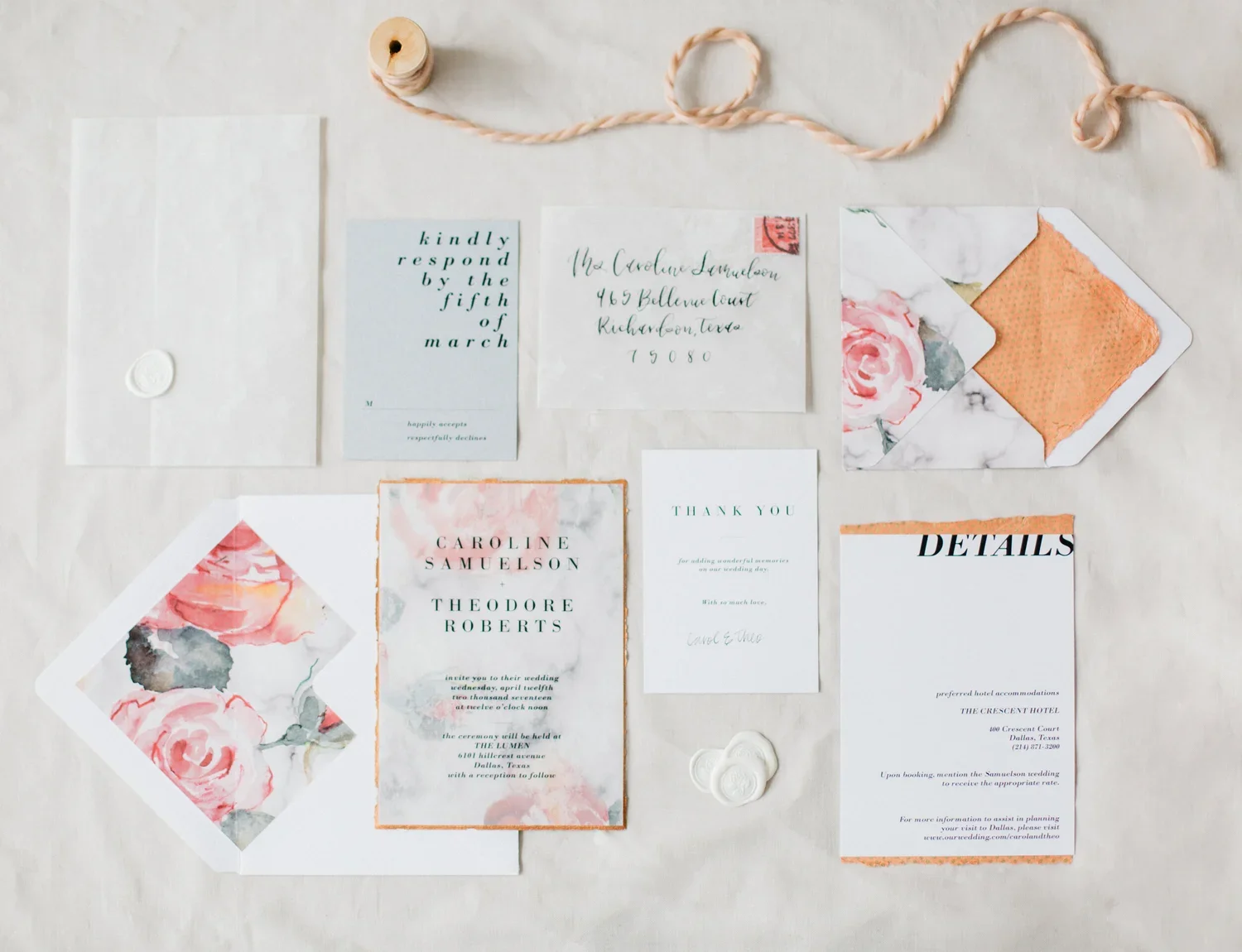 Collection of wedding stationery including invitations, RSVP card, thank you note, details card, and envelopes with floral and marble design, on a light fabric background, with a spool of peach-colored string.