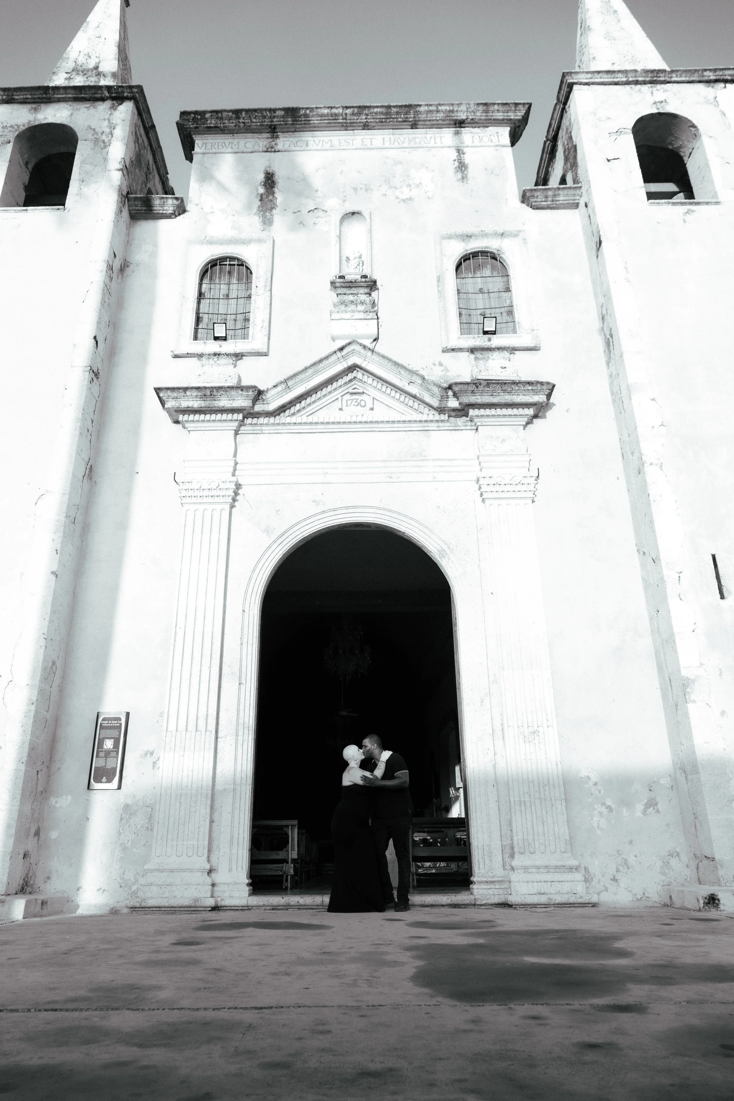 Couple dancing in front of a historic church building with an arched entrance, stone facade, and two bell towers, in black and white.