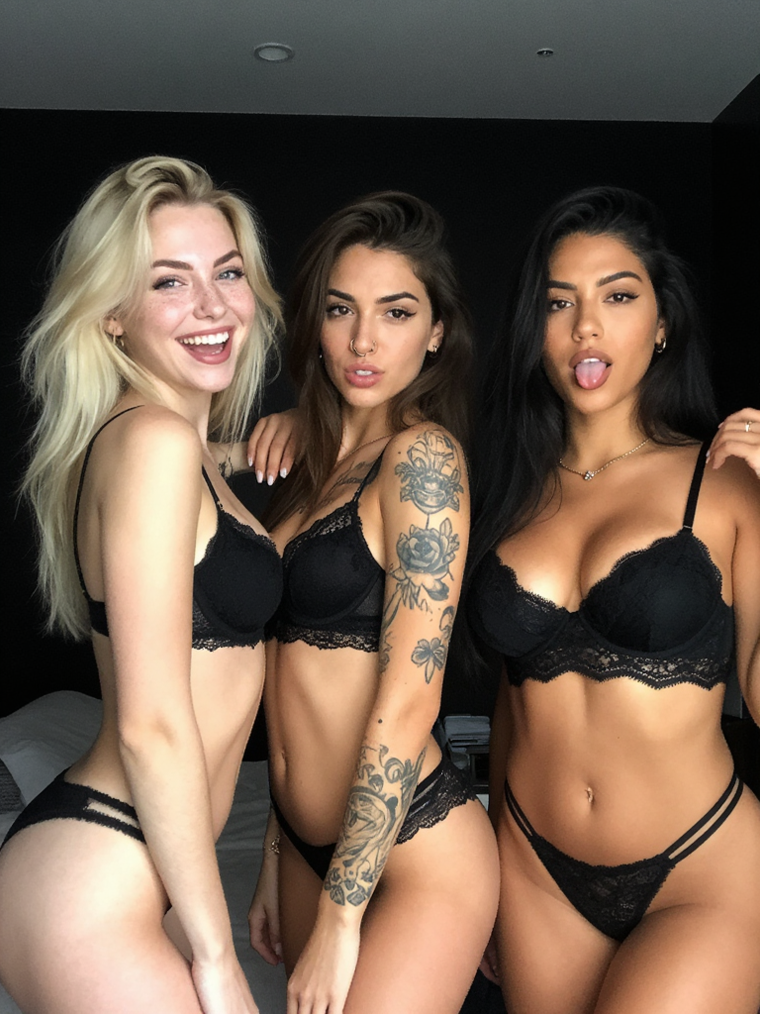 Three beautiful women strippers in black lace lingerie standing together in a room with a black background ready for the bachelor party.