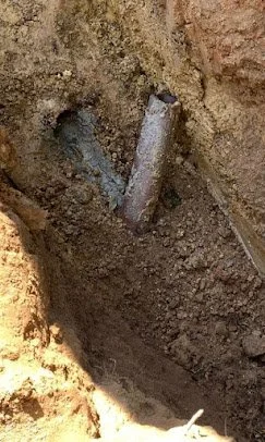 A partially buried metal pipe in a dug hole in the ground.