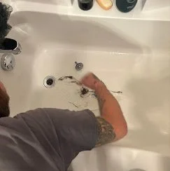 Person washing a brown dog in a white sink, holding the dog with one hand and using the other to clean it.