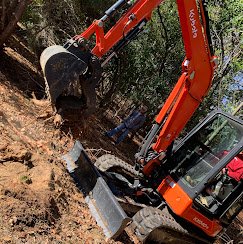 An orange excavator digging into a hillside or slope with trees in the background.
