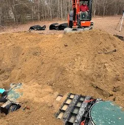 Construction site with an excavator and black tires, excavation tools, and a partially dug hole in the ground.