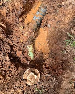 A drainage pipe in the ground with muddy water and a metal lid nearby.