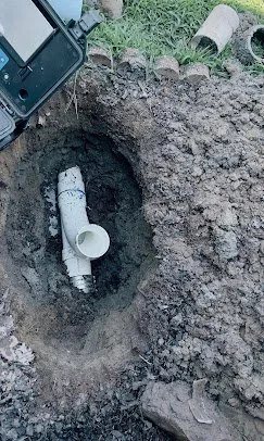 Close-up of a PVC pipe fitting in a dug hole in the ground during plumbing work.