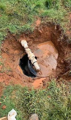 A pipe stuck in a muddy hole surrounded by grass.