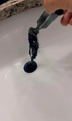 Hand holding a toothbrush with black toothpaste over a sink drain.