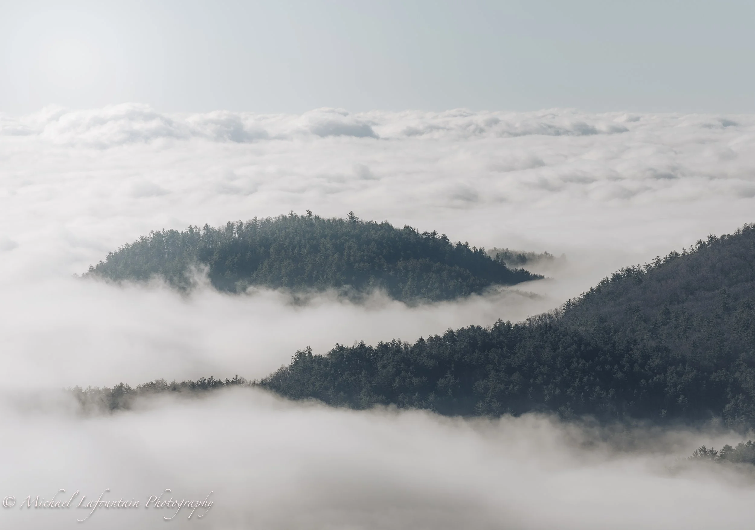 Mountain landscape with forested peaks emerging above clouds and fog.