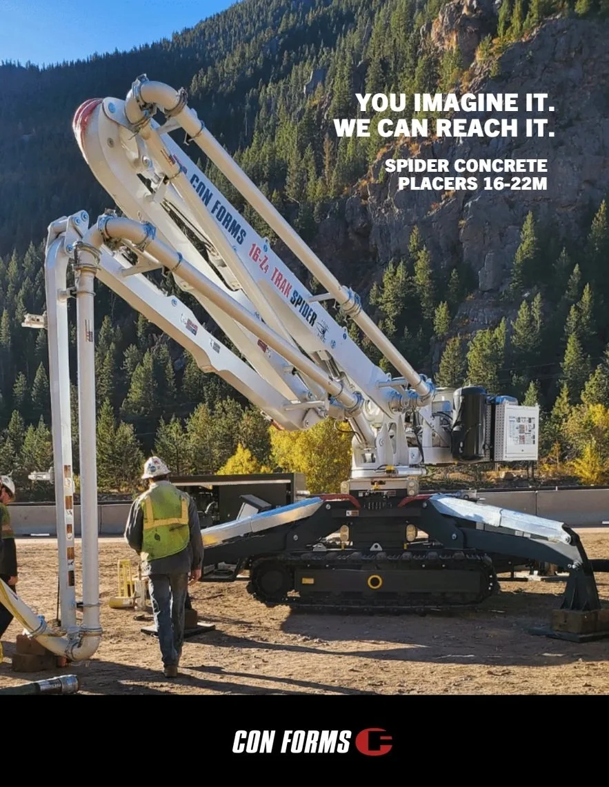 Construction workers at a site with a large spider concrete track mounted placer, set against a backdrop of trees and mountains.