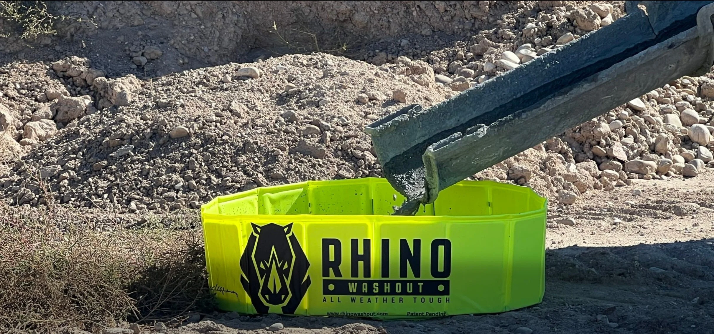 A construction site with concrete being poured into a bright yellow Rhino Concrete Washout container, 'RHINO WASHOUT ALL WEATHER TOUGH'.