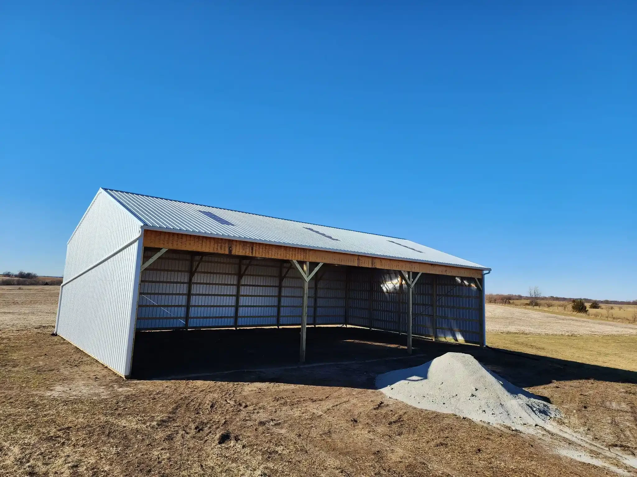 A metal shed with a sloped roof on open land under a clear blue sky