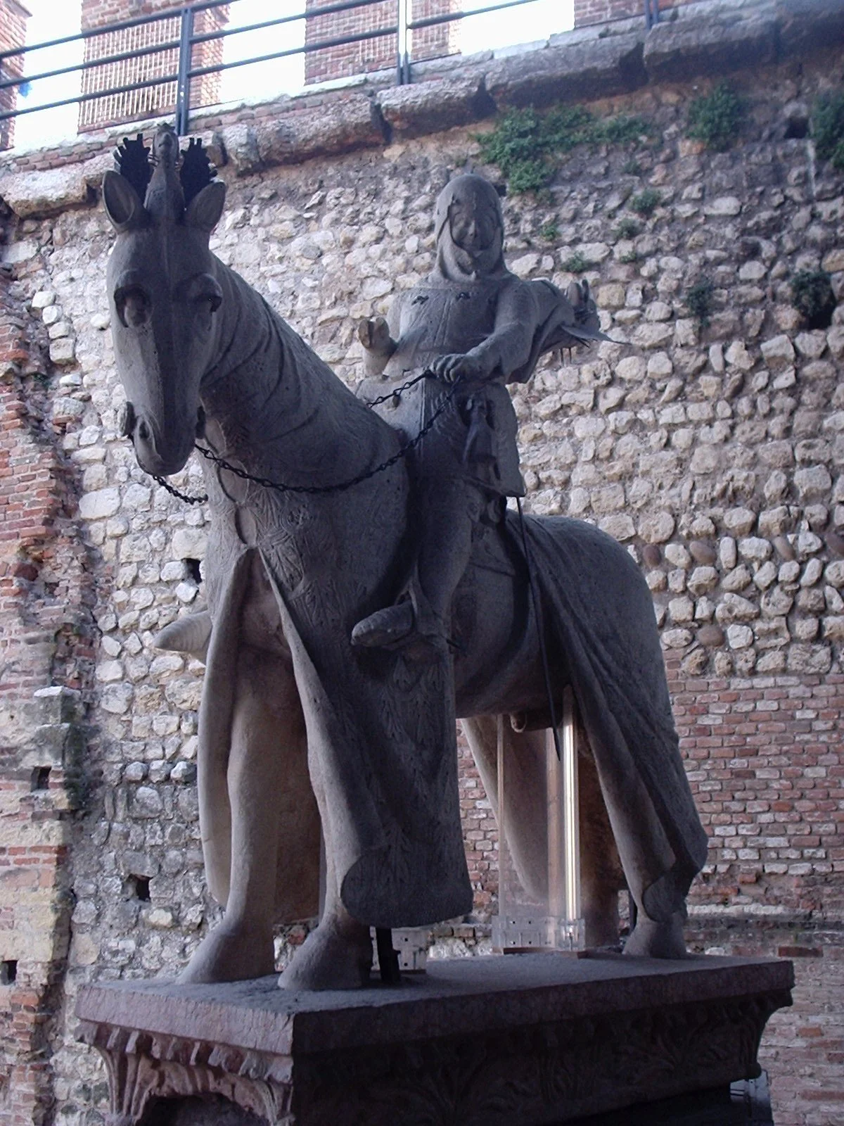 A bronze sculpture of a man riding a horse, set against a brick and stone wall background.