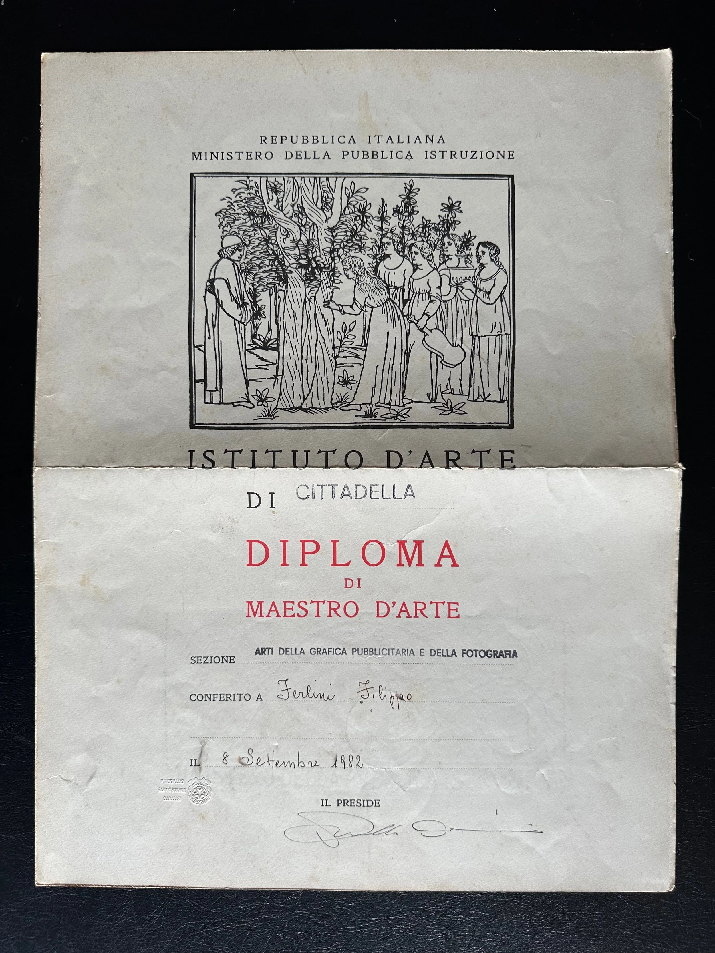 An Italian diploma certificate from 1982 with text and a black-and-white illustration of people gathered around a tree, possibly in an outdoor setting.