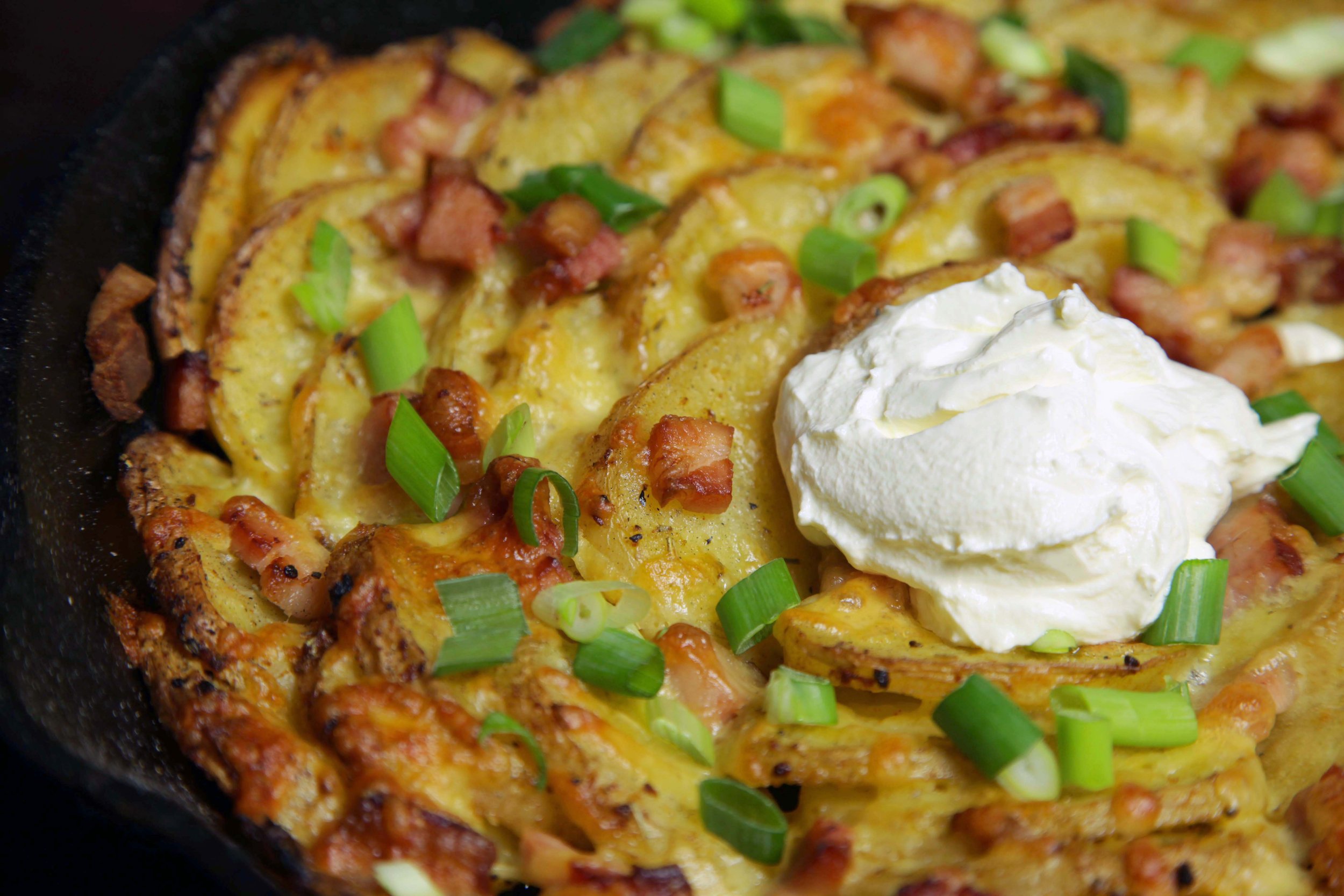 Close-up of breakfast skillet with scrambled eggs, diced bacon, green onions, and a dollop of sour cream.