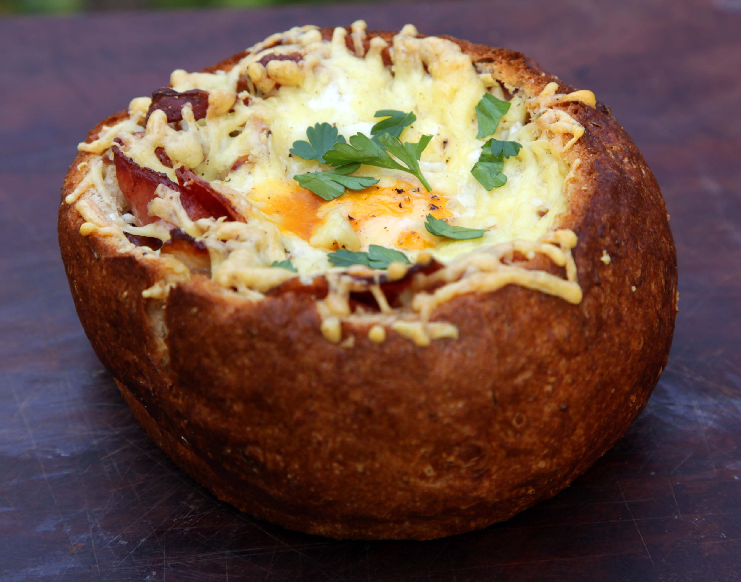 Baked bread bowl filled with cheesy mashed potatoes, bacon, and a baked egg, garnished with parsley.