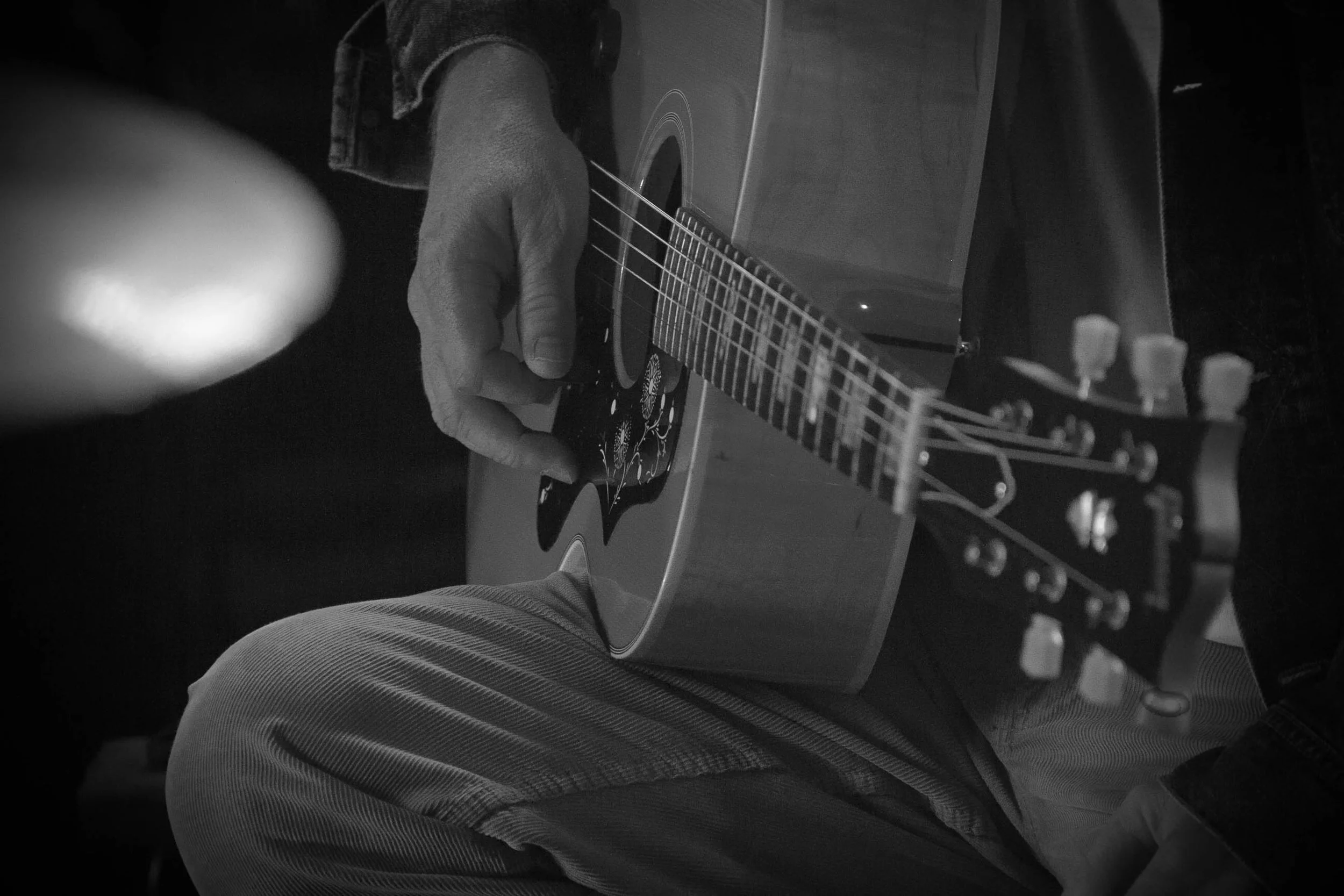 A person playing an acoustic guitar with their left hand on the fretboard, while sitting down.