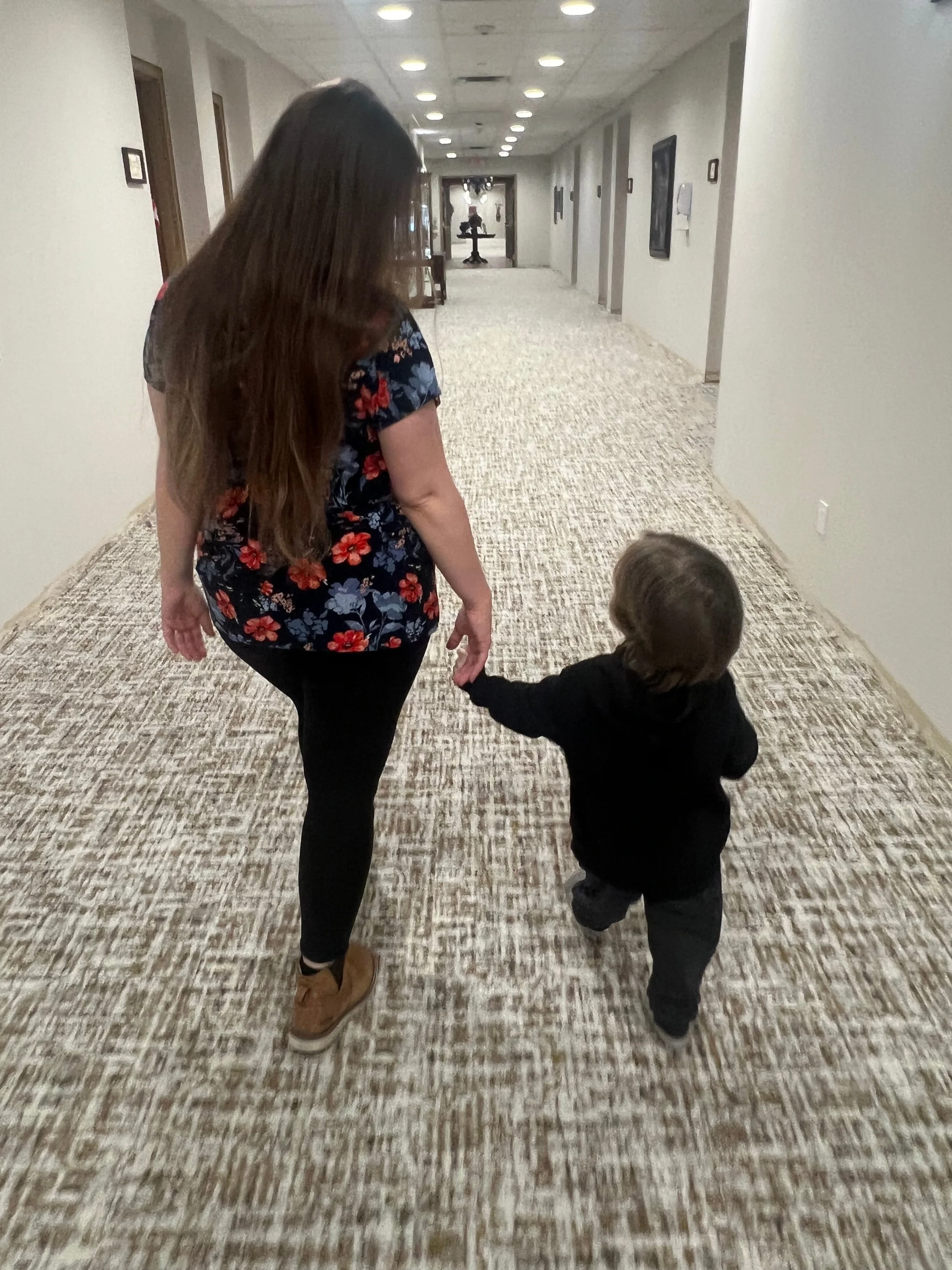 A woman holding hands with a young child walking down a hotel corridor.