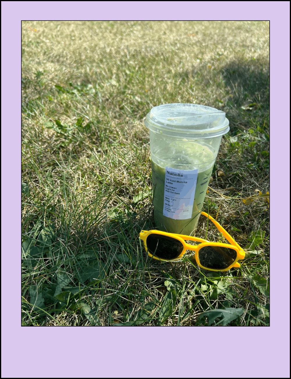 A partially consumed iced matcha latte in a transparent cup with a lid, resting on grass with a pair of yellow sunglasses nearby.