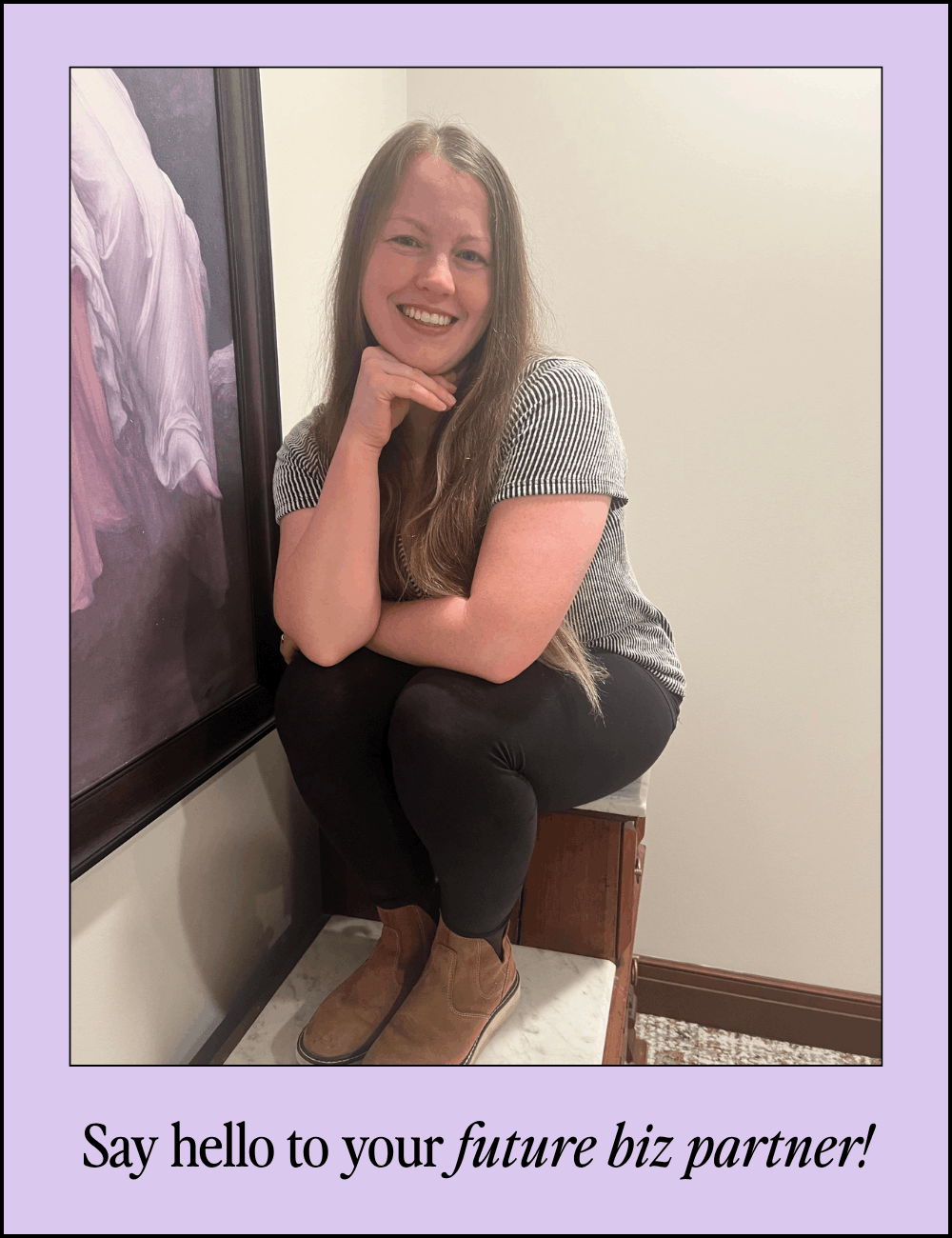 Smiling woman with long hair, sitting on a small wooden cabinet in front of a plain wall and a framed painting, wearing a striped shirt, black pants, and brown boots, with her right hand resting on her chin and left arm crossed over her lap. Caption reads: "Say hello to your future biz partner!"