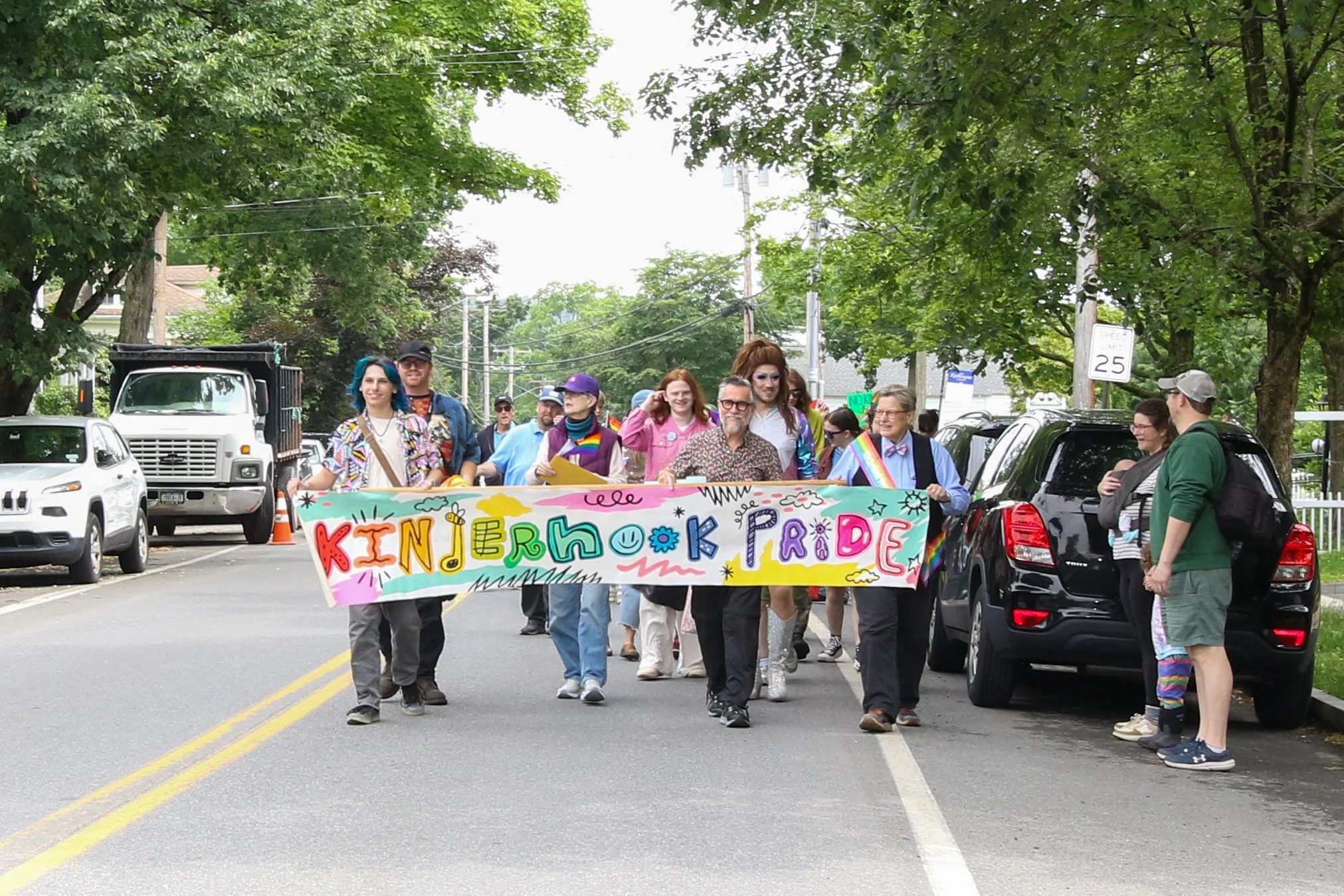 A group of people marching in a pride parade holding a colorful banner that says 'Kinderhook Pride'.