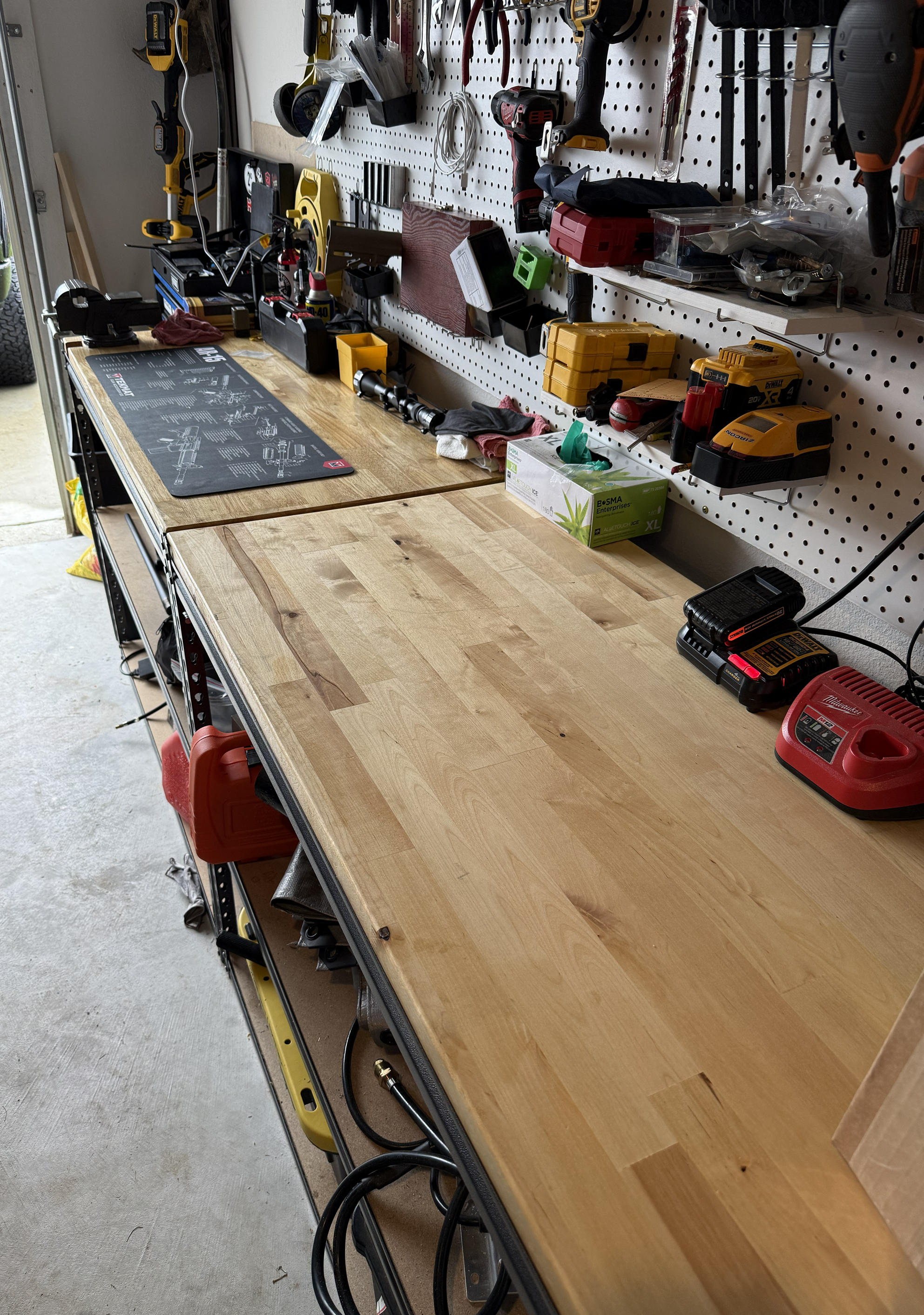 A workbench with various tools and equipment, including power drills, a measuring tape, a saw, and a box of gloves, with a pegboard for hanging tools in a garage or workshop.