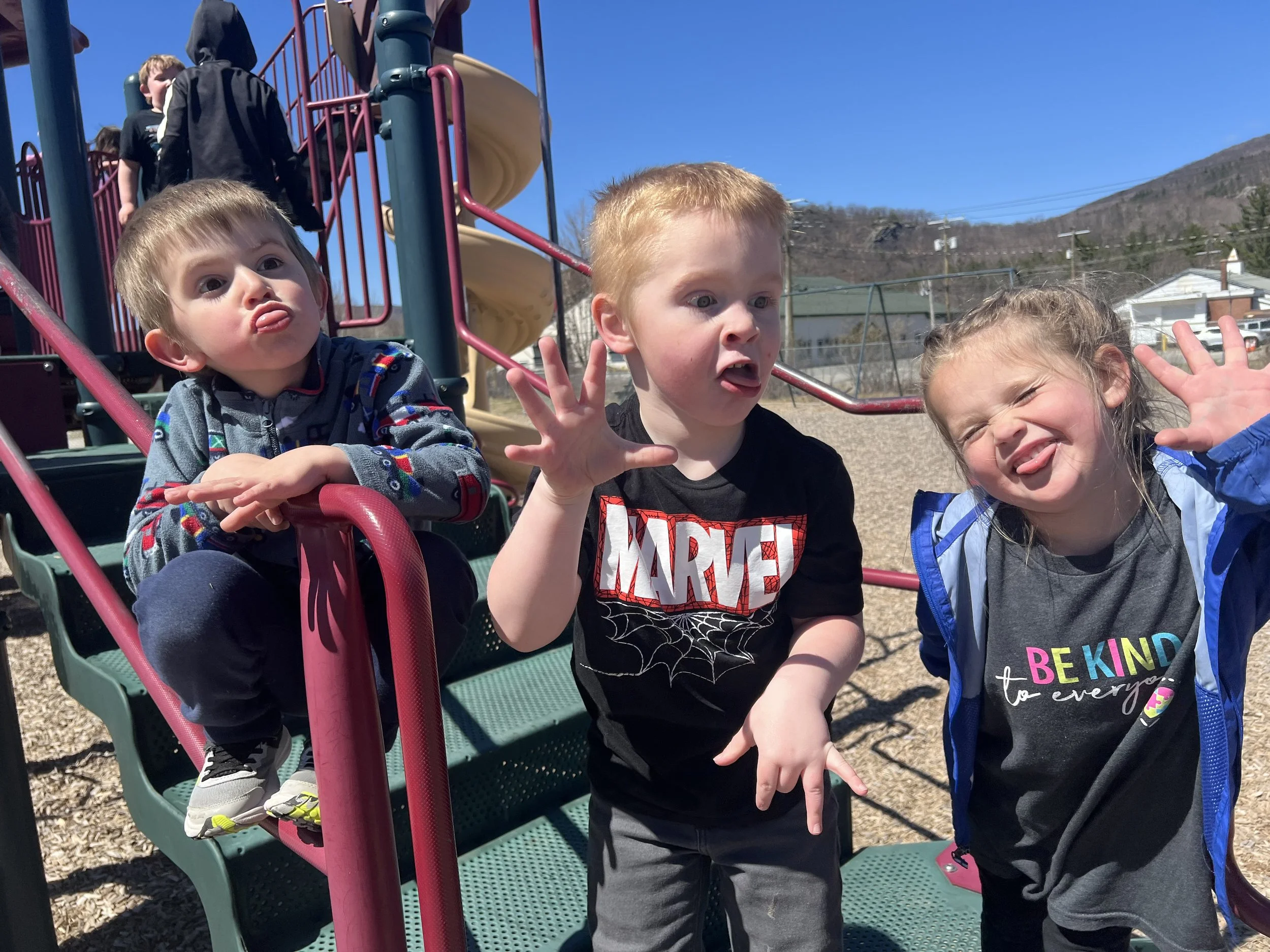 Young children playing on a playground slide on a sunny day.