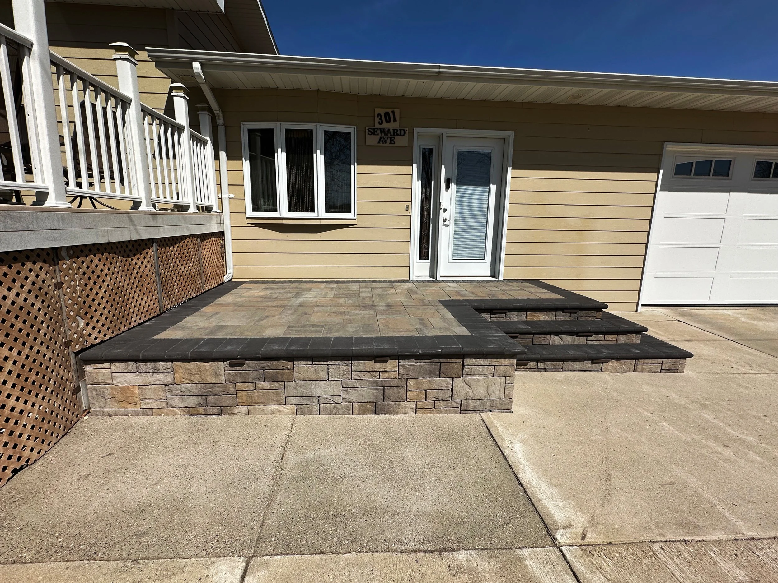 Front entrance of a house with a small porch, stone steps, and a white door, beige siding, a window with white trim, and a sign with address number 301 on Seward Ave.