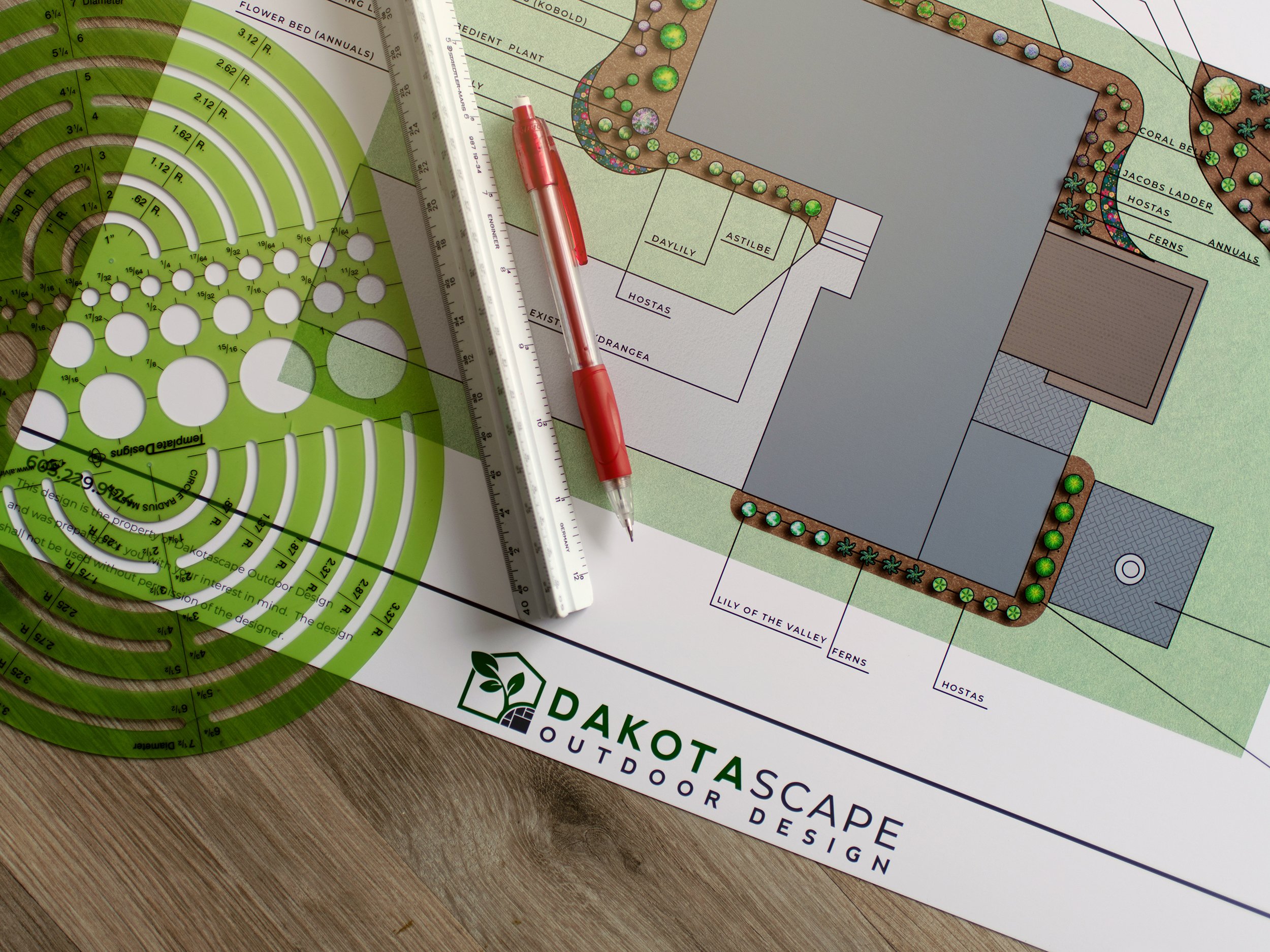 Landscape architecture plan with a green garden layout, a red pen, a triangular ruler, and a landscaping template. The plan is titled 'Dakota Scape Outdoor Design' and includes various garden features and plant labels.