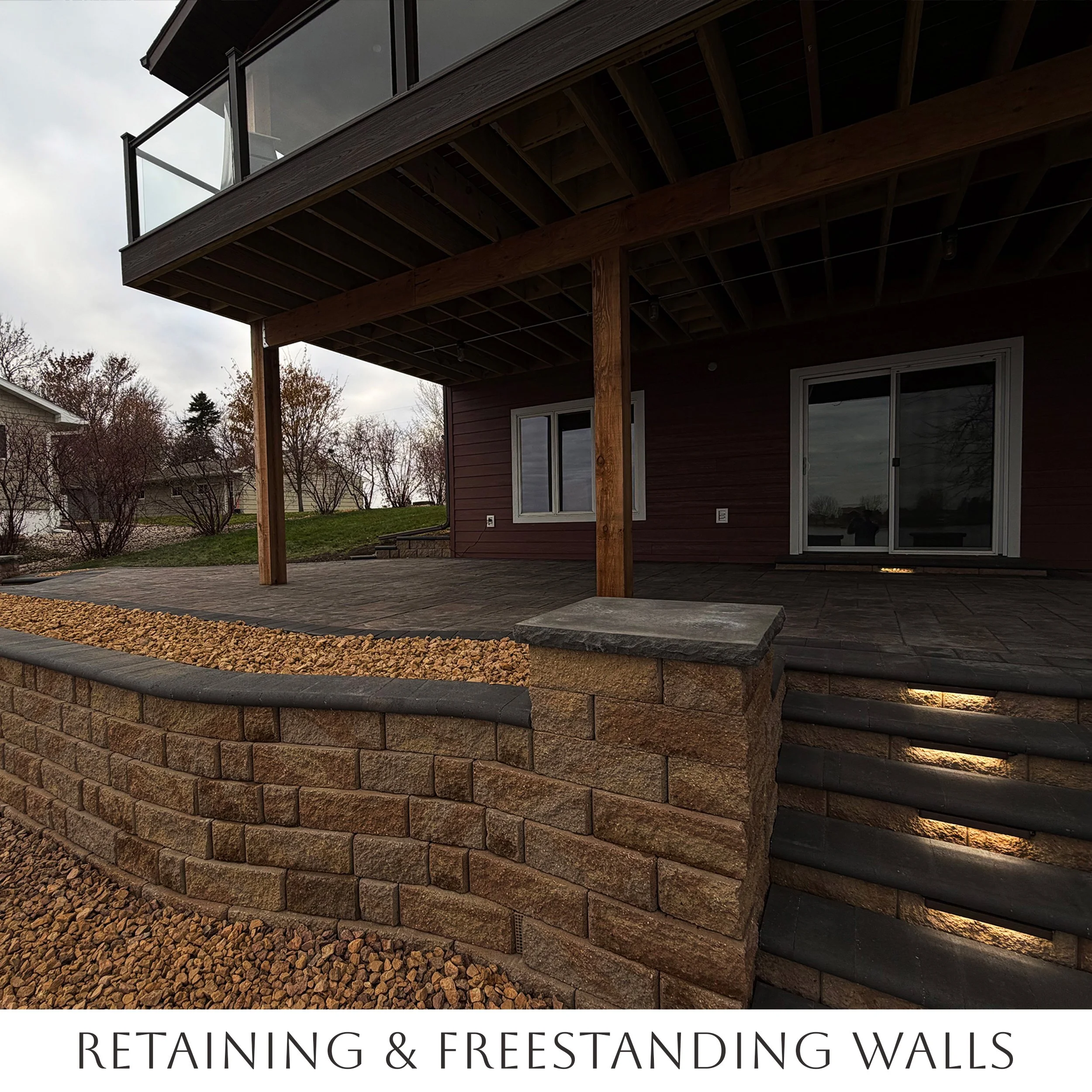 Exterior view of a house patio featuring retaining walls and freestanding walls, with gravel and stone accents.