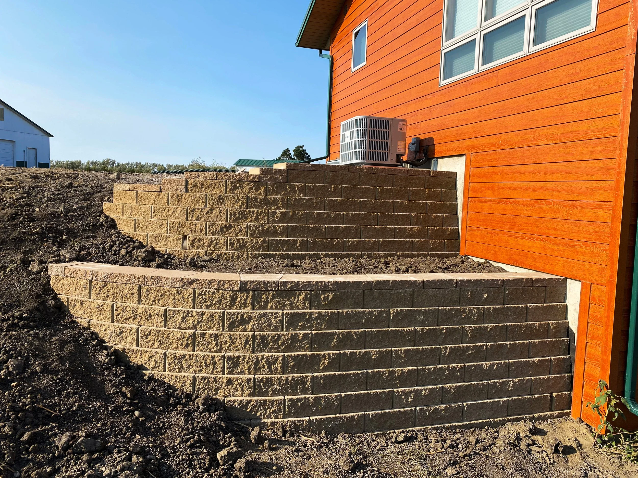 Newly built brick patio with stairs outside a house with orange siding and a heat pump unit on the ground