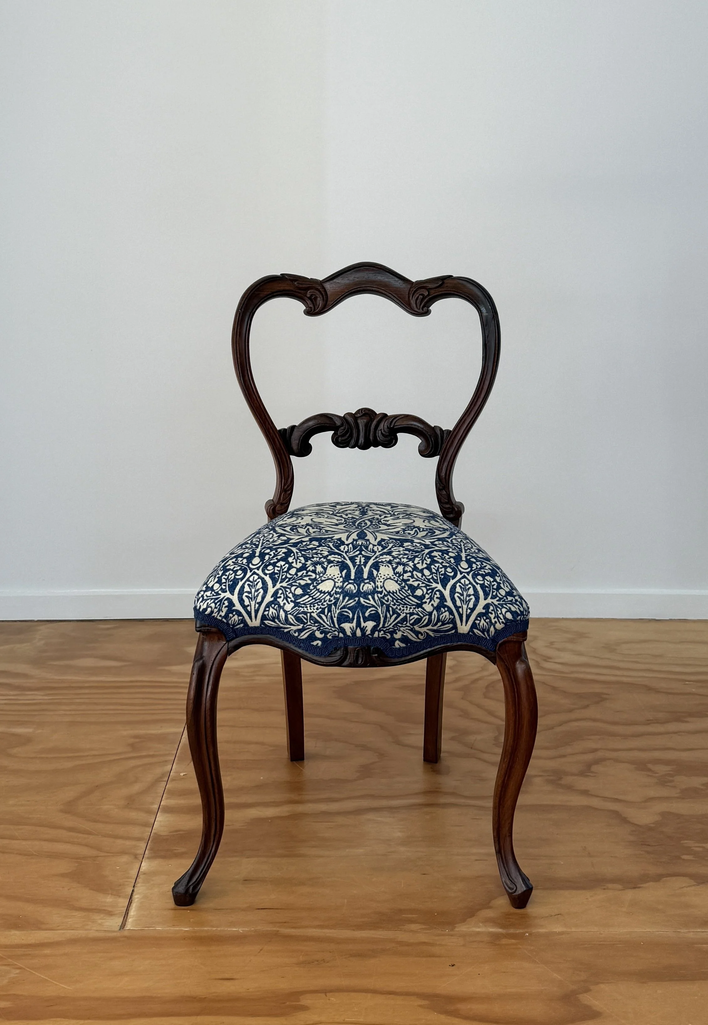 An antique wooden chair with a carved heart-shaped backrest and blue and white floral upholstery on the seat.
