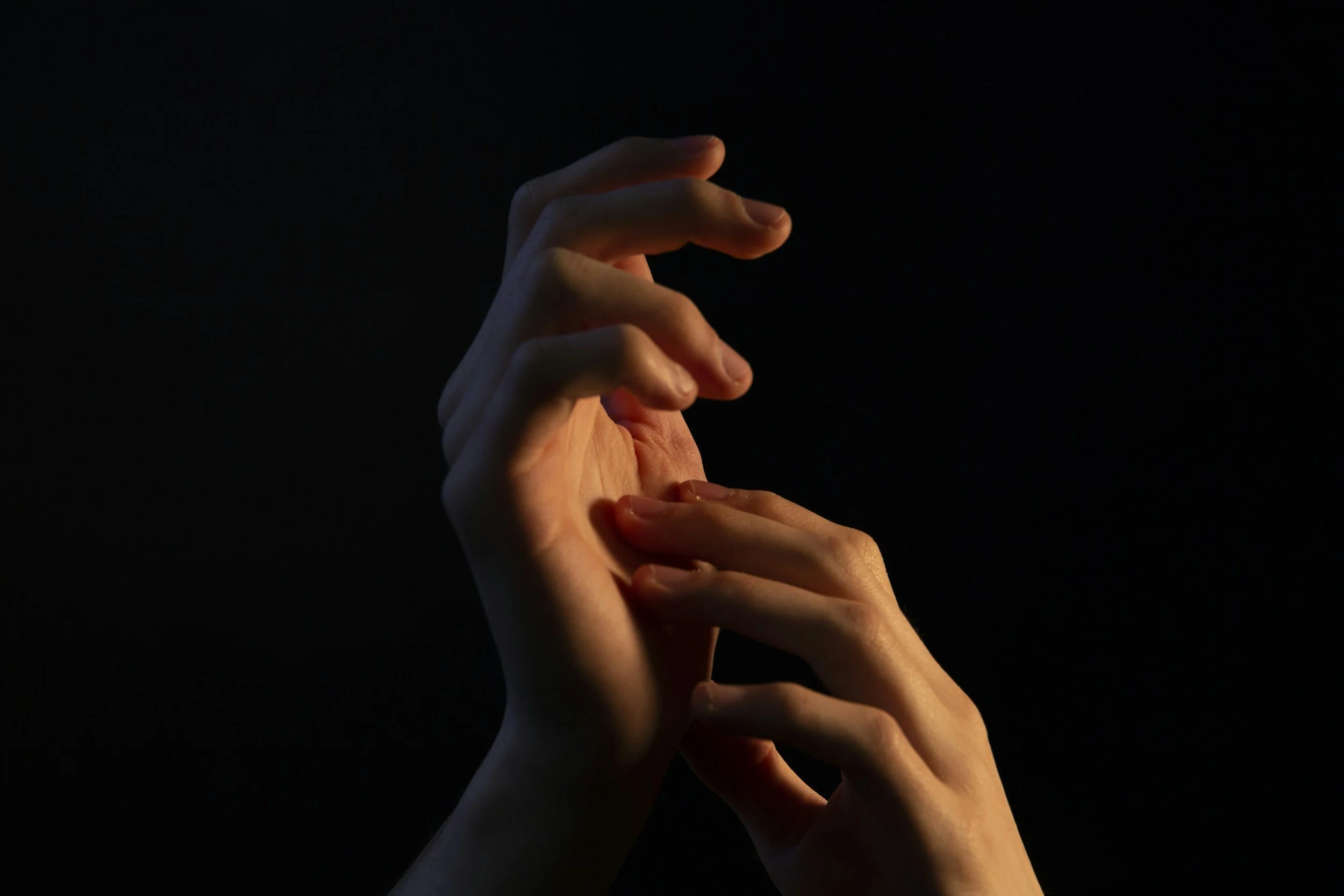 Two gentle hands reaching out and touching each other against a dark background.
