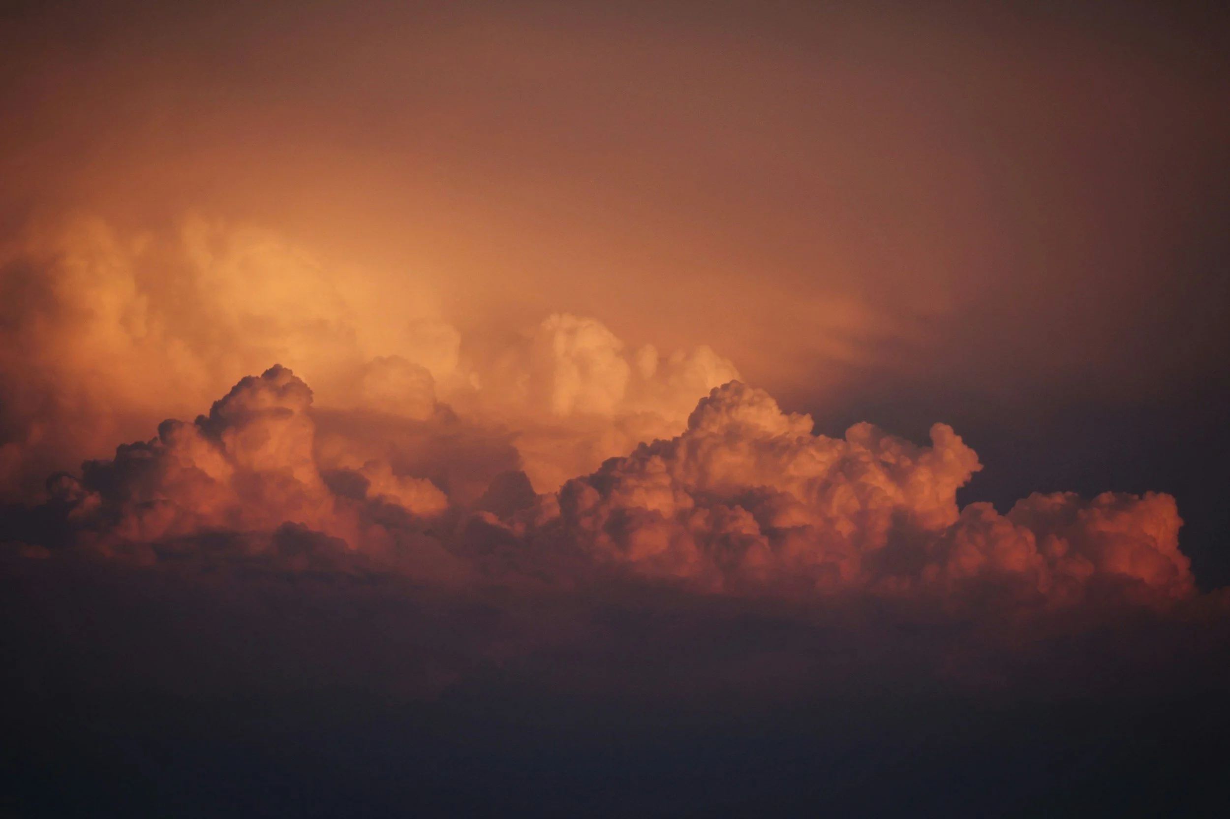 A dramatic sky with large, billowing clouds glowing with orange and pink hues during sunset or sunrise.