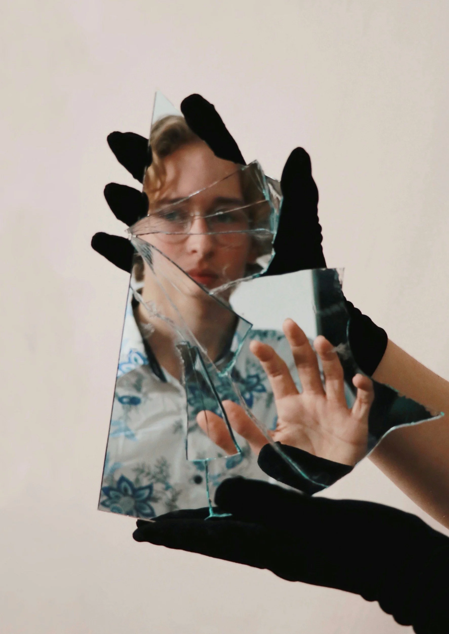 Person holding a broken mirror with a face reflection, wearing black gloves.