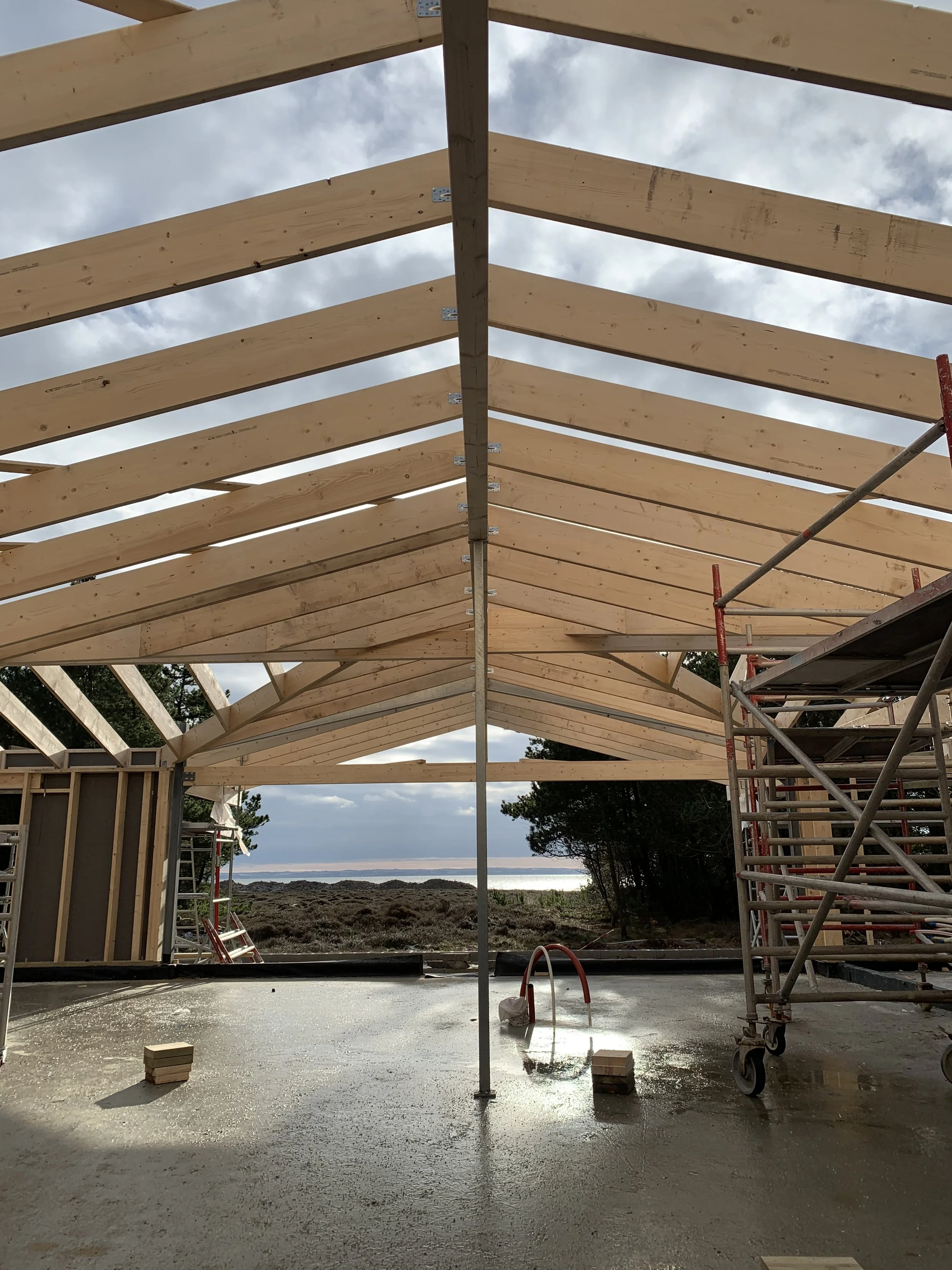 Bygningsramme under konstruktion med træbjælker og scaffolding, udsigt til hav og natur