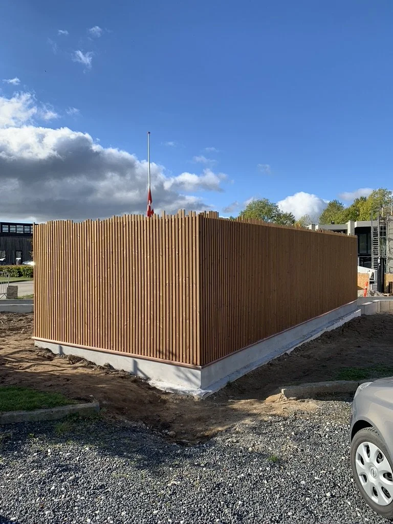 En bygning med træpaneler udendørs under en blå himmel med nogle skyer, og en svenskerflagg på en flagstang.