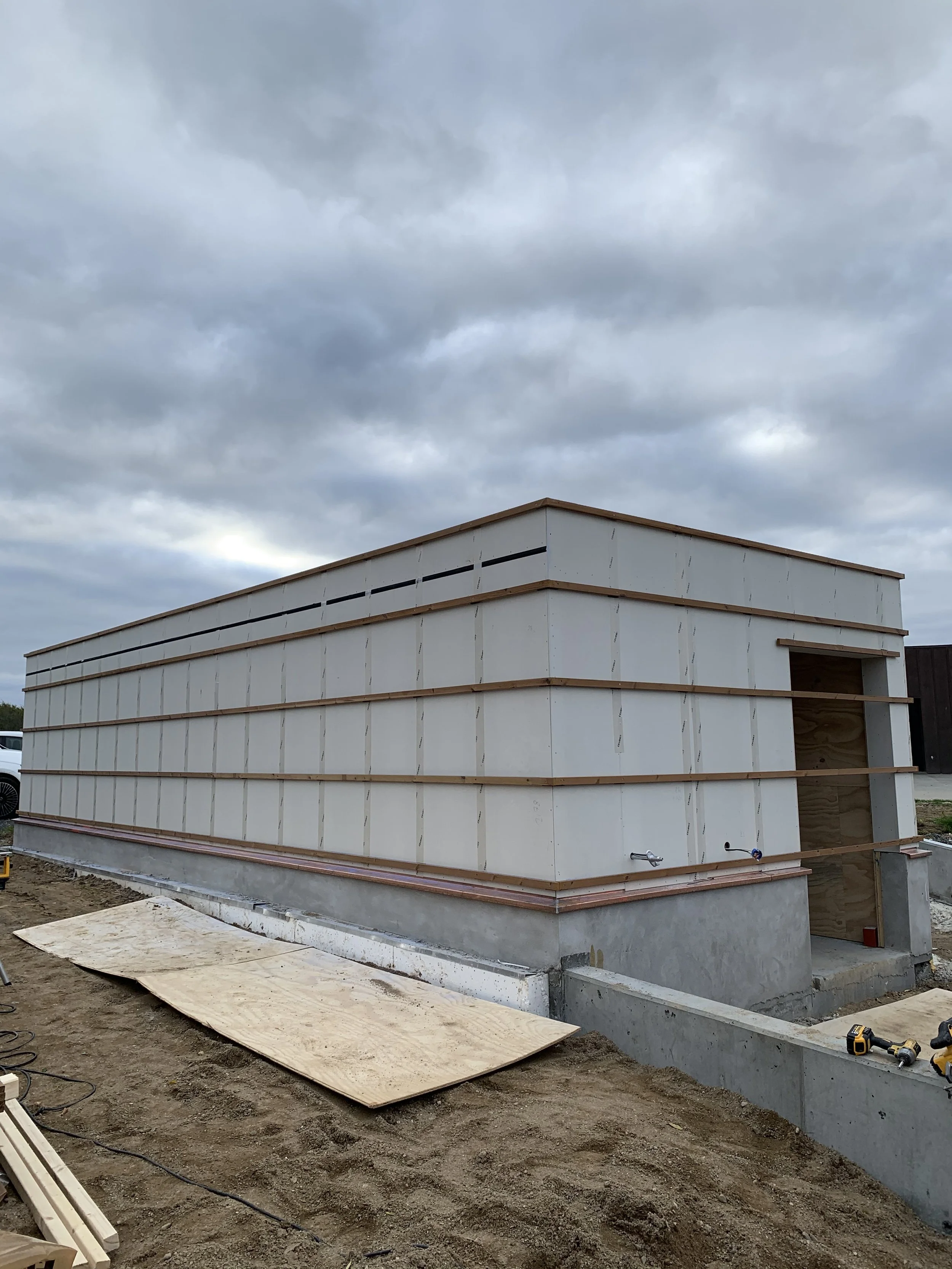 Et byggeri under opførelse med en grundmur i beton og et træskelet, omgivet af byggematerialer og værktøj.
