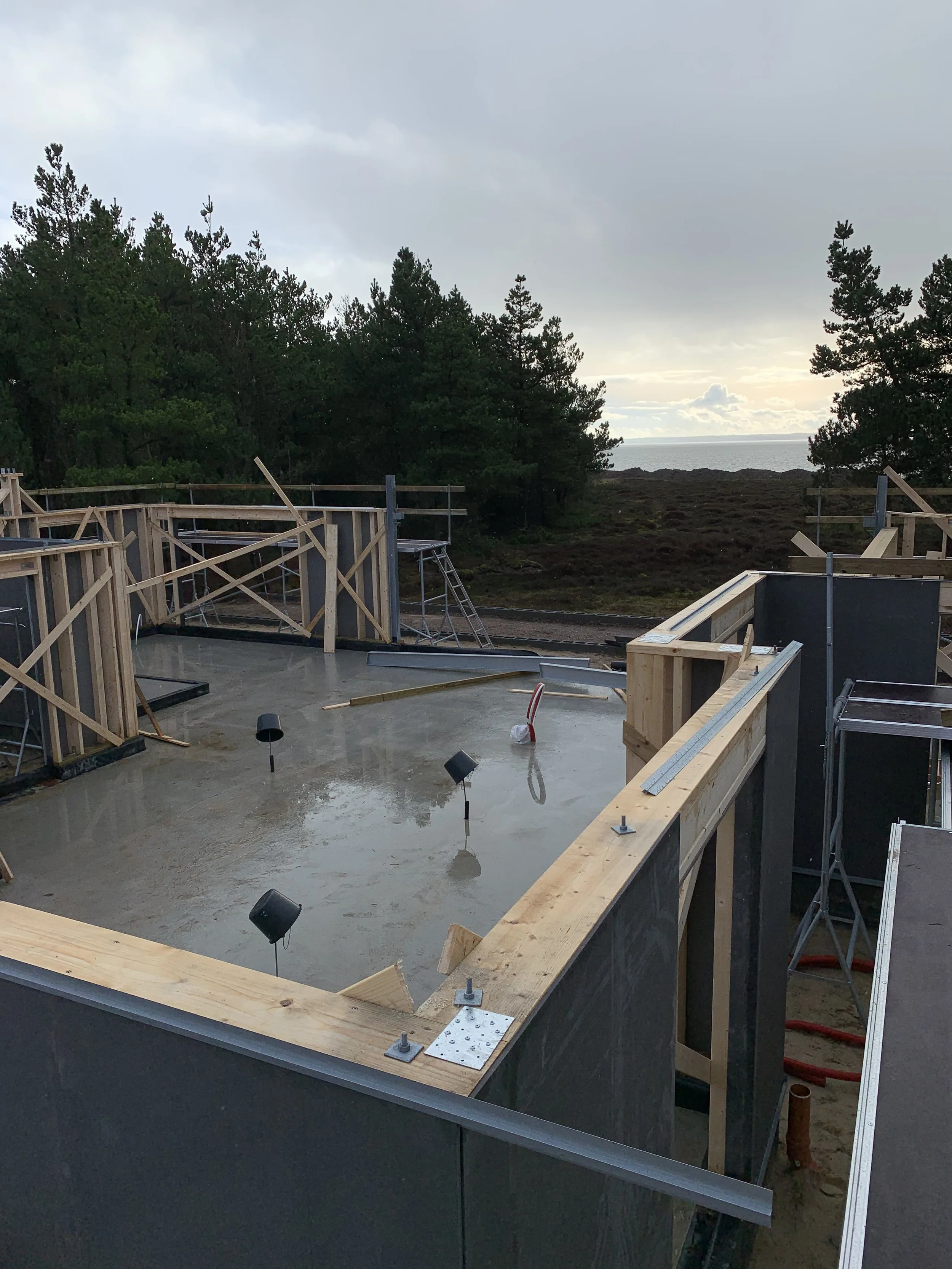 Byggerod af træ og beton, med udsigt over hav og træer i baggrunden.