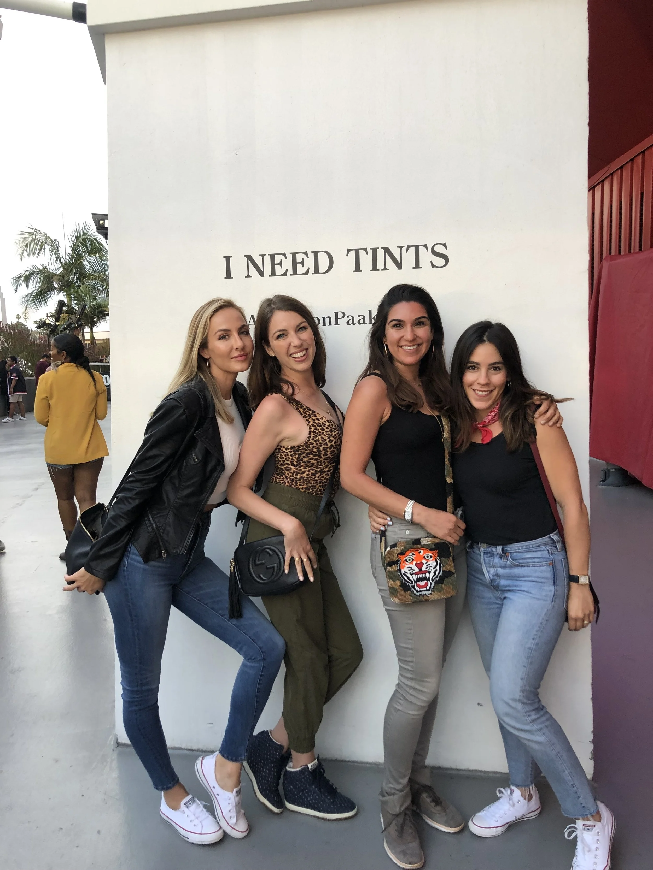 Boxing babes standing in front of a white wall at an Anderson Paak concert in Los Angeles. They are all smiling and dressed casually.