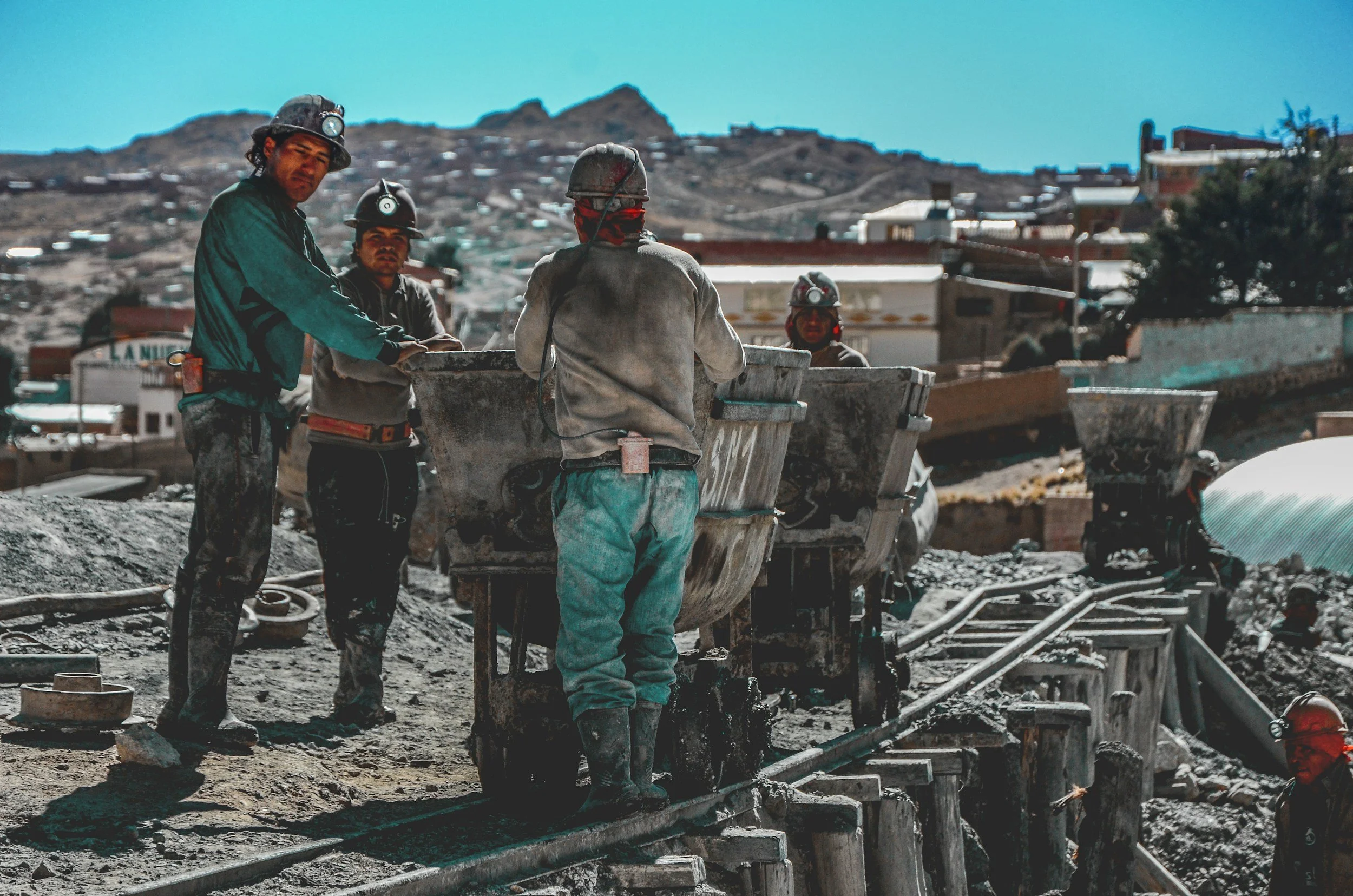 Coal miners working underground, wearing helmets with lights, standing next to carts on railway tracks in a mining site.