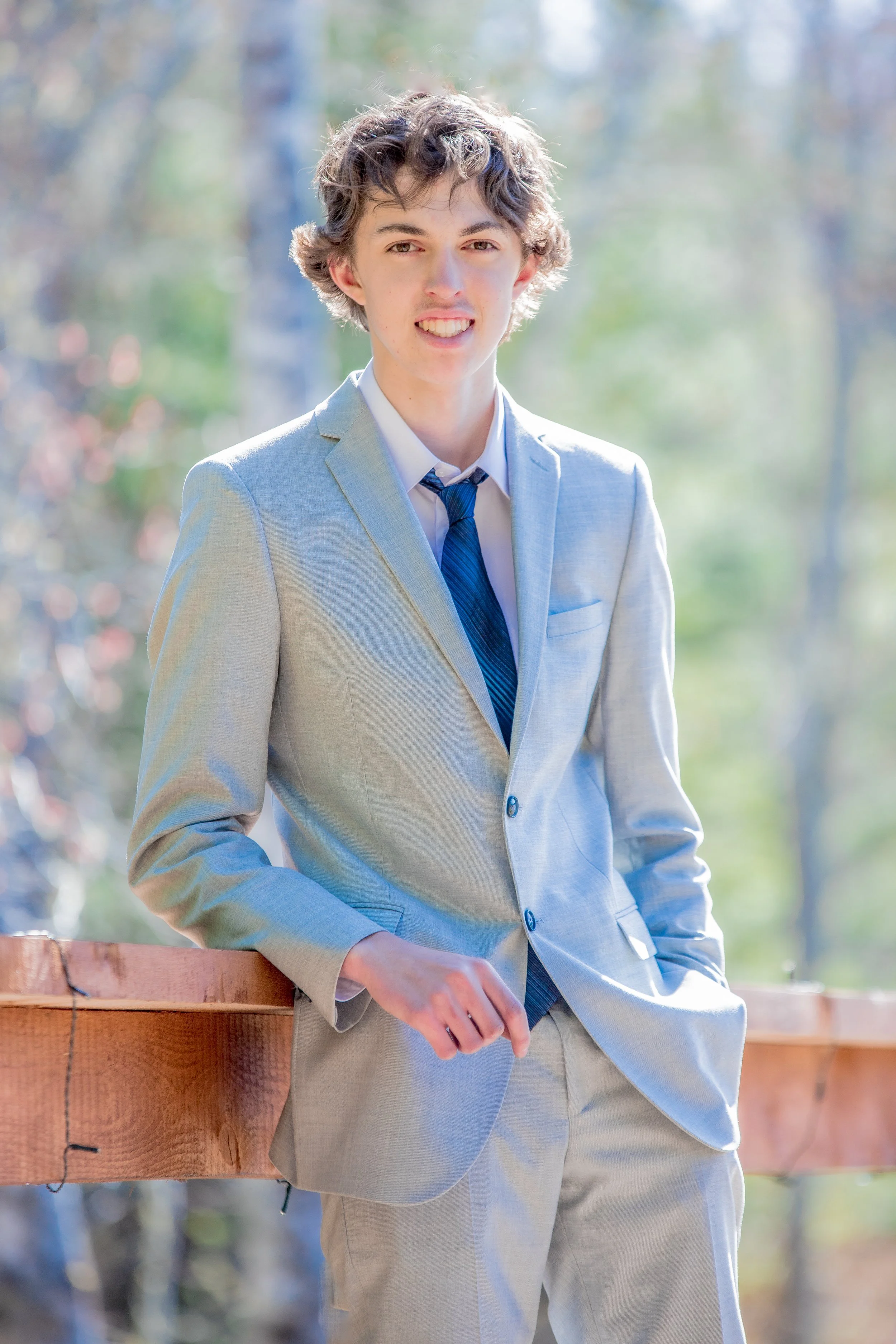 Lucas MacDonald, owner of PrimeCutServices in a light gray suit outdoors, smiling with hand in pocket, blurred trees in background.