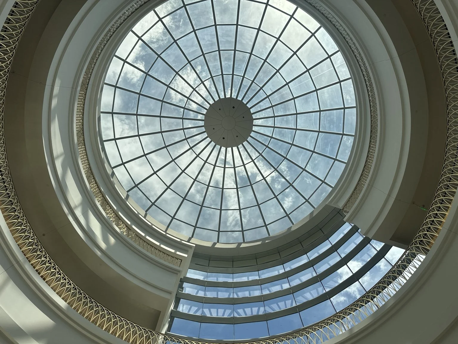 View of a glass-domed ceiling with a circular structure and sky visible through the glass.