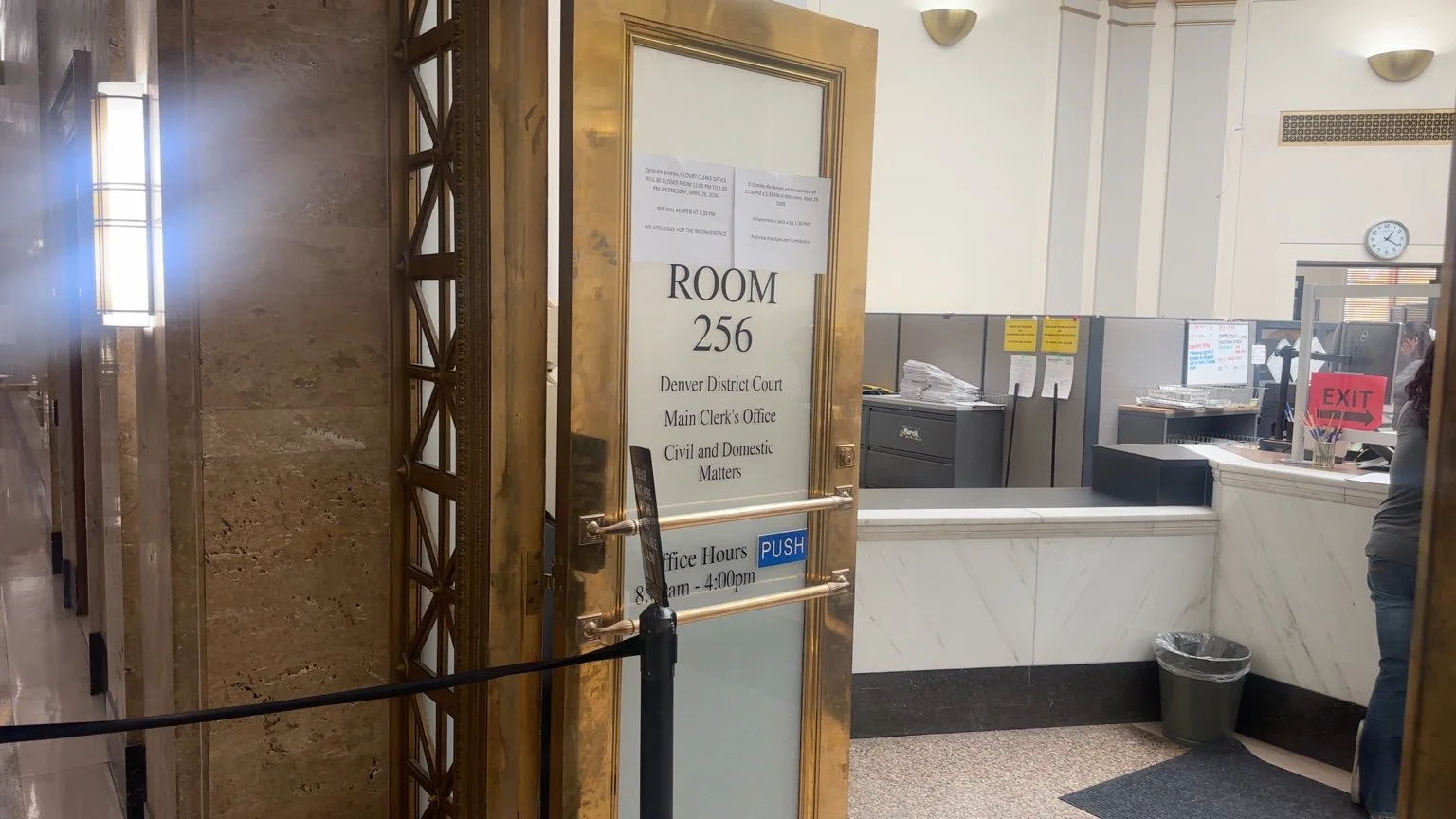 Entrance to Room 256 at Denver District Court Main Clerk's Office with sign displaying office hours and notice, marble counter and a person at the reception desk.