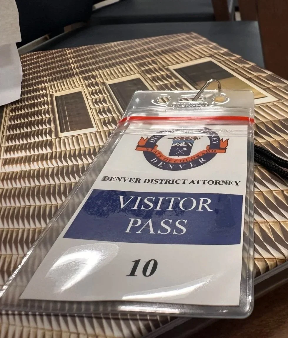 Visitor pass for the Denver District Attorney's Office, placed on a table with a photo collage.