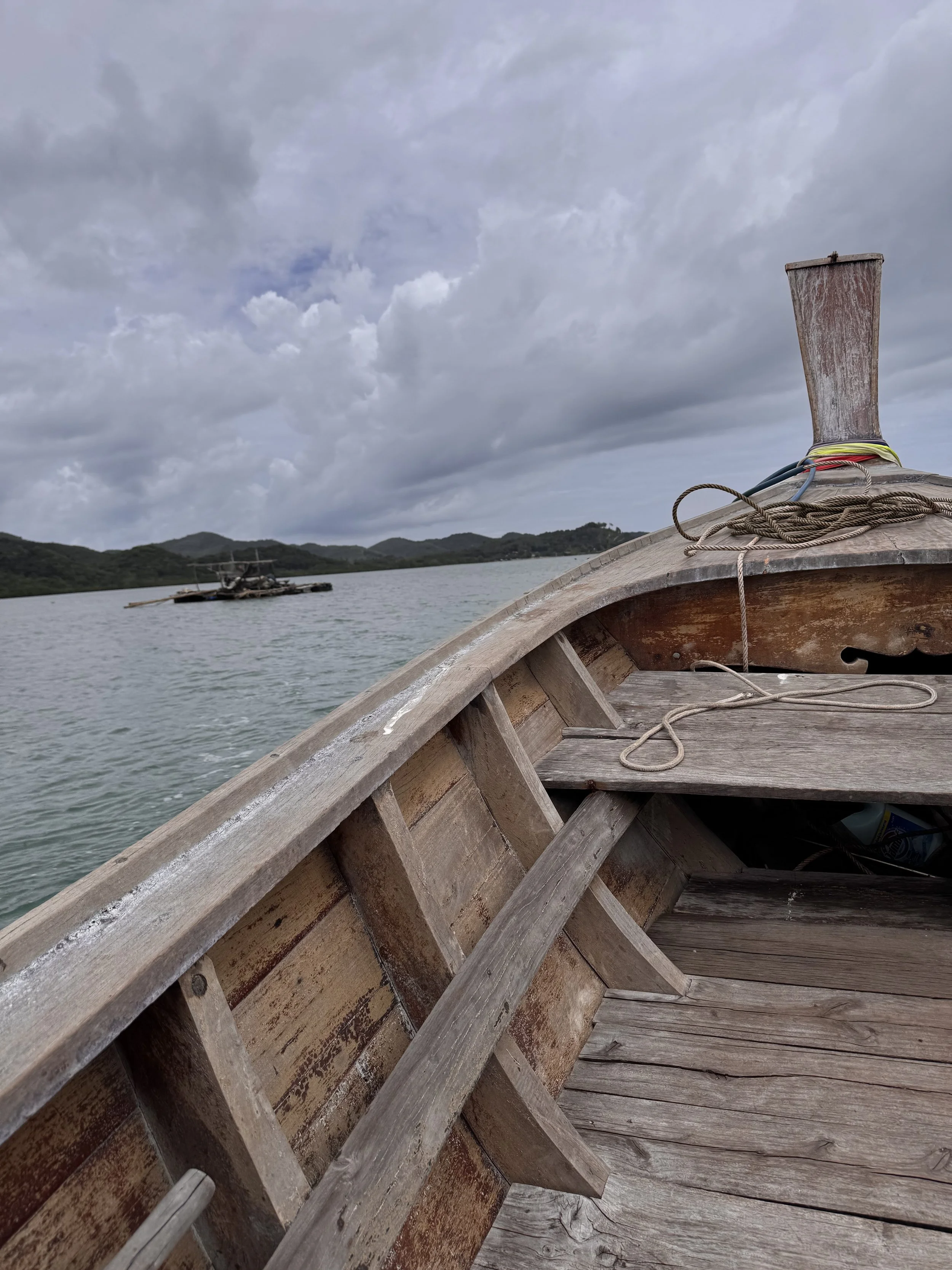 View of a wooden boat on a body of water with mountains and cloudy sky in the background.