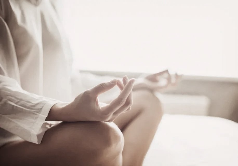 Person sitting on a bed in a lotus position practicing meditation or yoga, with hands in a mudra gesture.