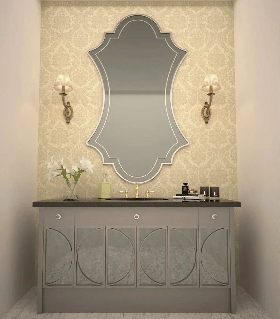 Bathroom vanity with a large decorative mirror, two wall sconces, a vase with white lilies, and a few small containers and books on the countertop in a softly illuminated space.