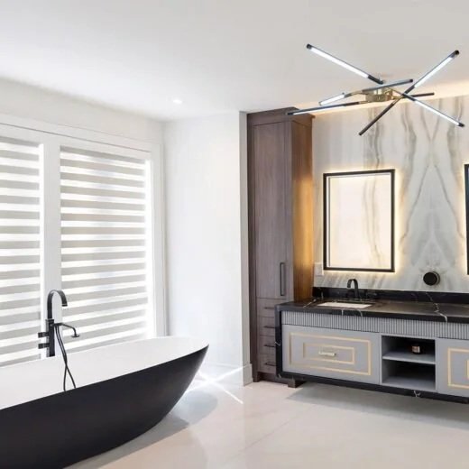 Modern bathroom with a black freestanding bathtub, a large window with striped blinds, a marble wall, a wooden cabinet, a sleek vanity with a mirror, and a contemporary chandelier.