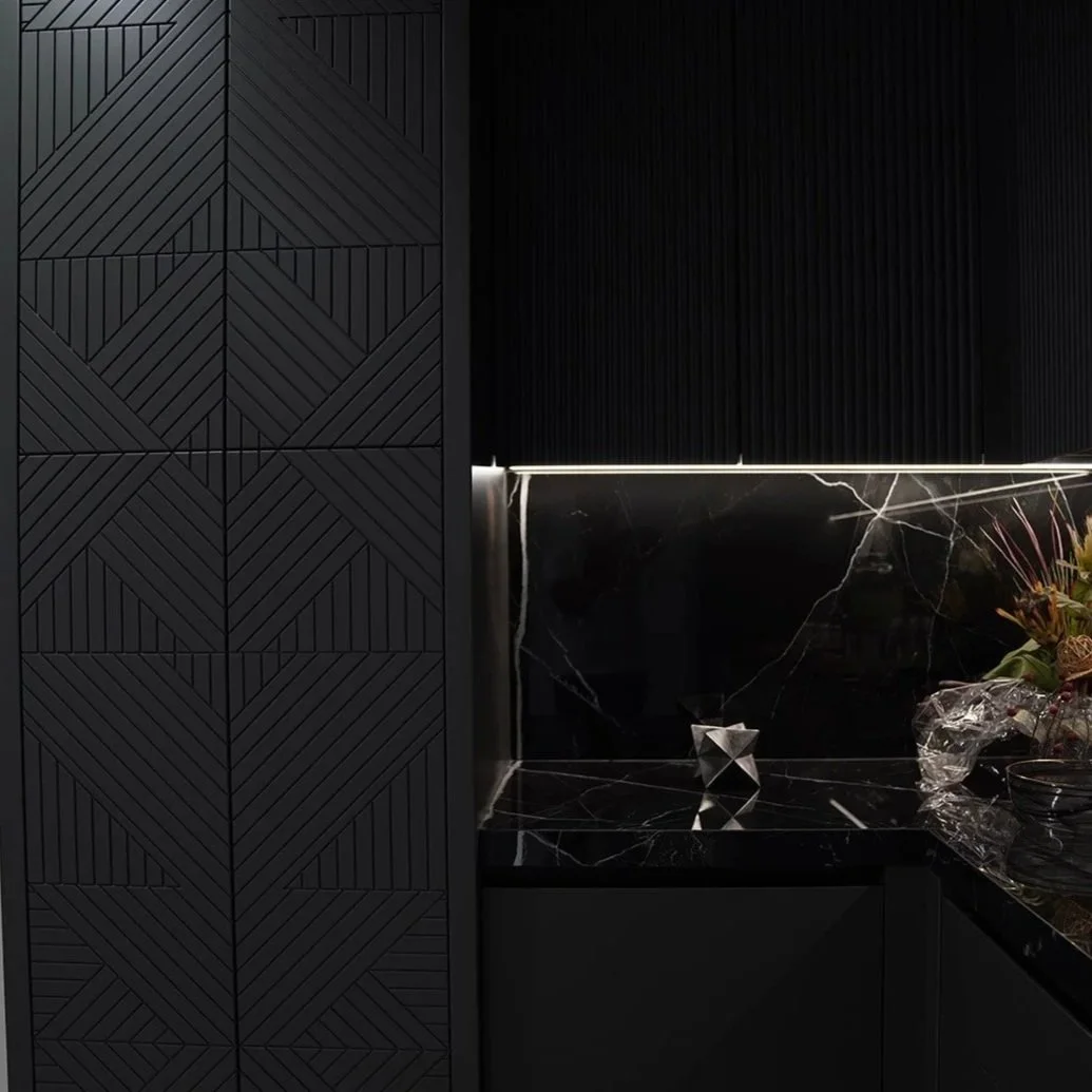 A modern interior kitchen with black cabinetry, black marble countertops, and geometric textured black wall panels.